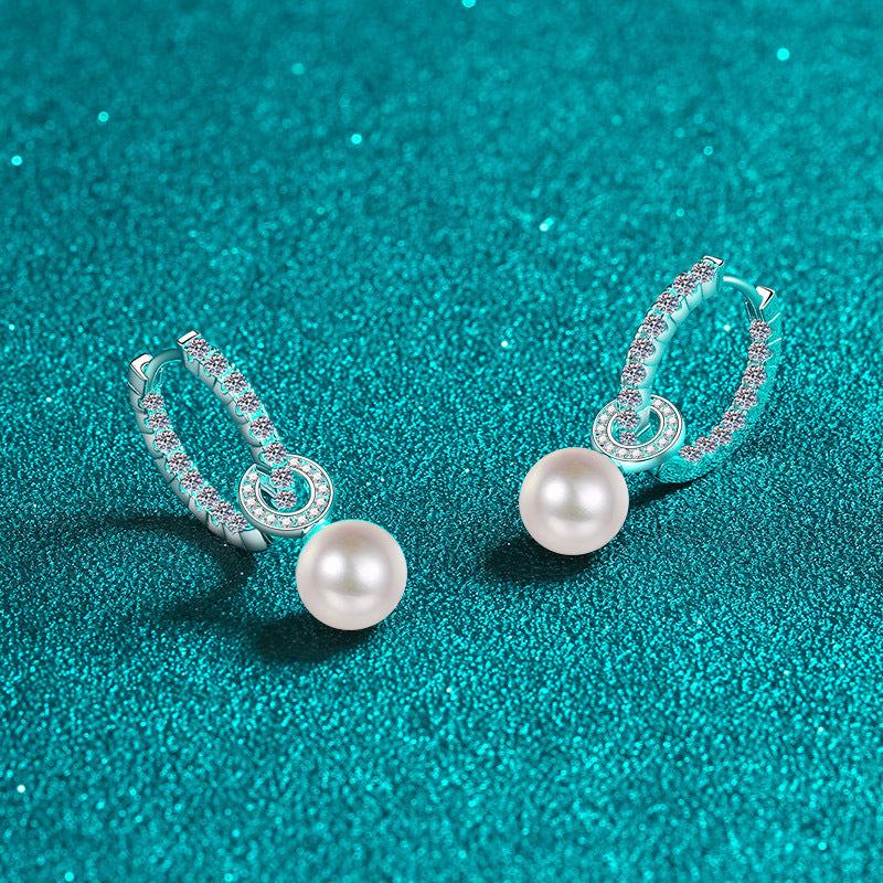 Pair of pearl earrings with silver hoop designs on a teal glitter background
