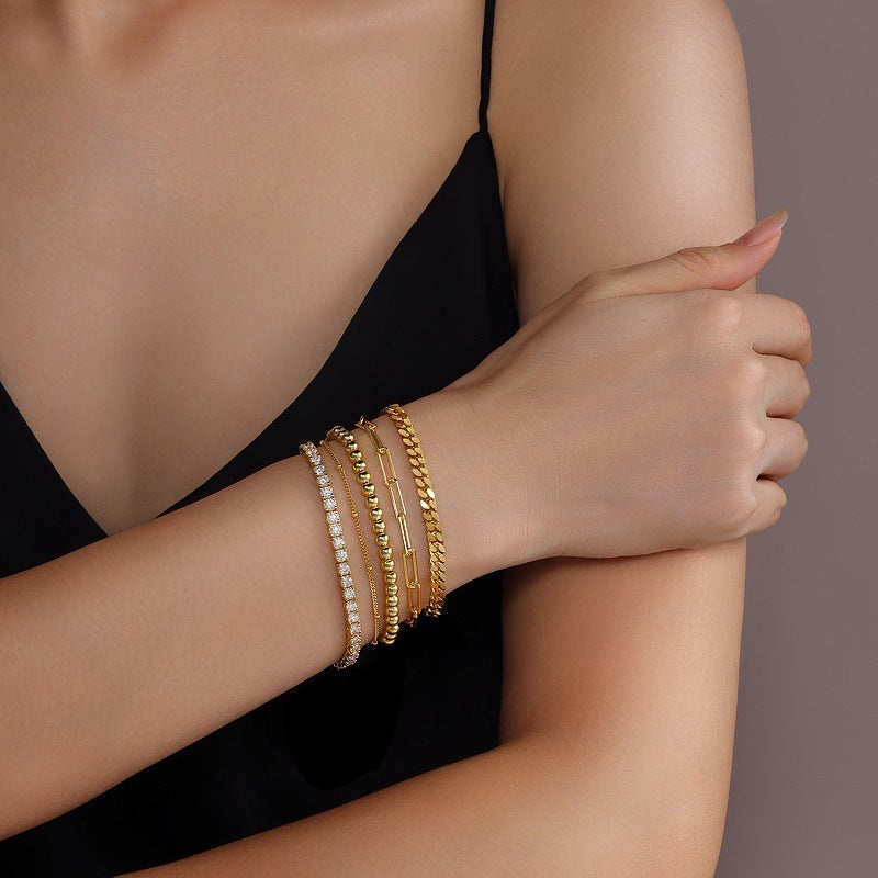 Woman's arm wearing multiple gold bracelets on a neutral background