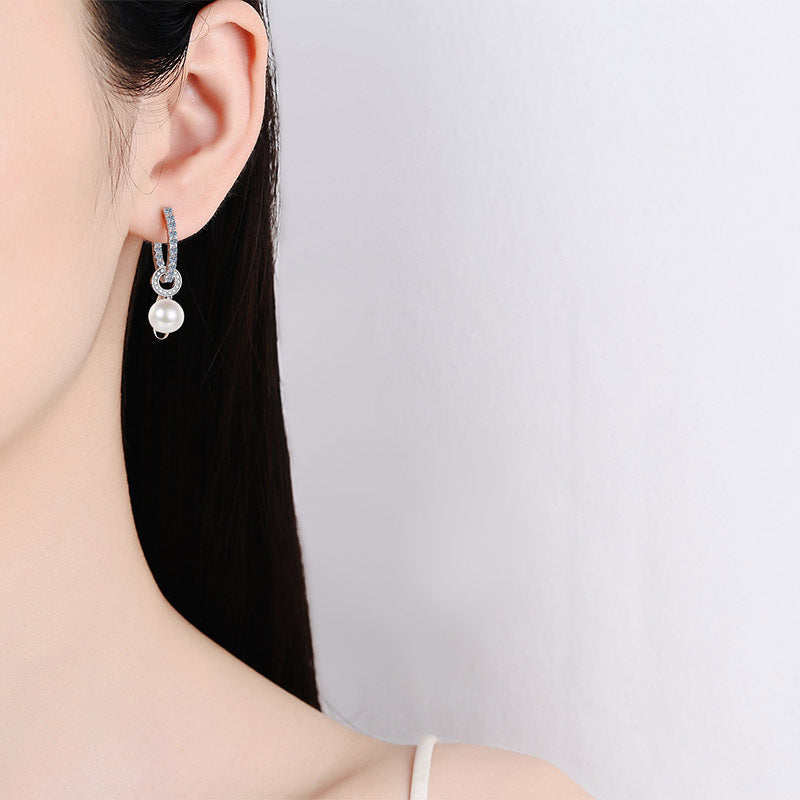 Close-up of a woman wearing a silver earring with a pearl on a plain background